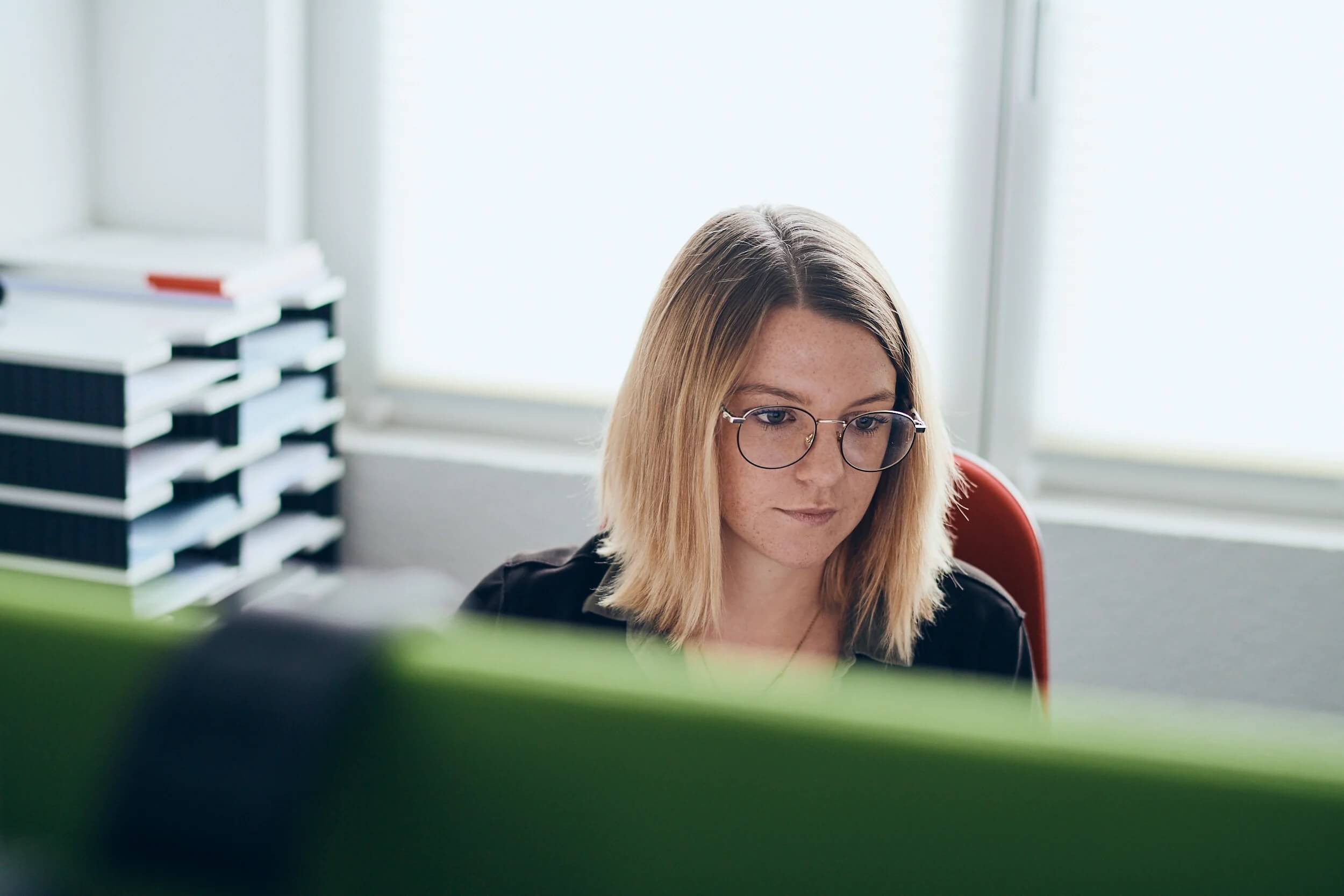 Stellenanzeige Marketing: Bild von Frau mit Brille, die an Schreibtisch an einem Computer sitzt und im Marketing arbeitet 